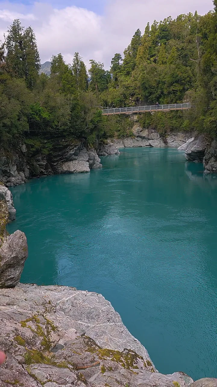 Turquoise river water below a footbridge, surrounded by bush