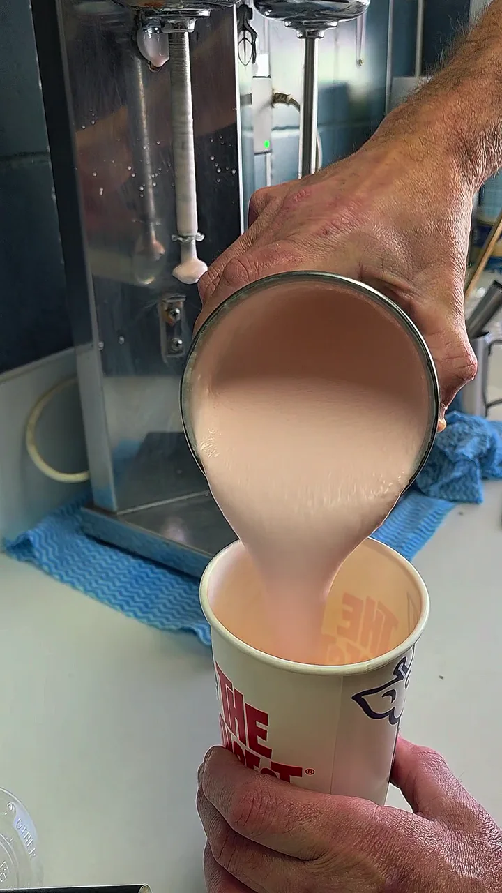 A freshly mixed pink milkshake being poured into a Triple B Burgers cup